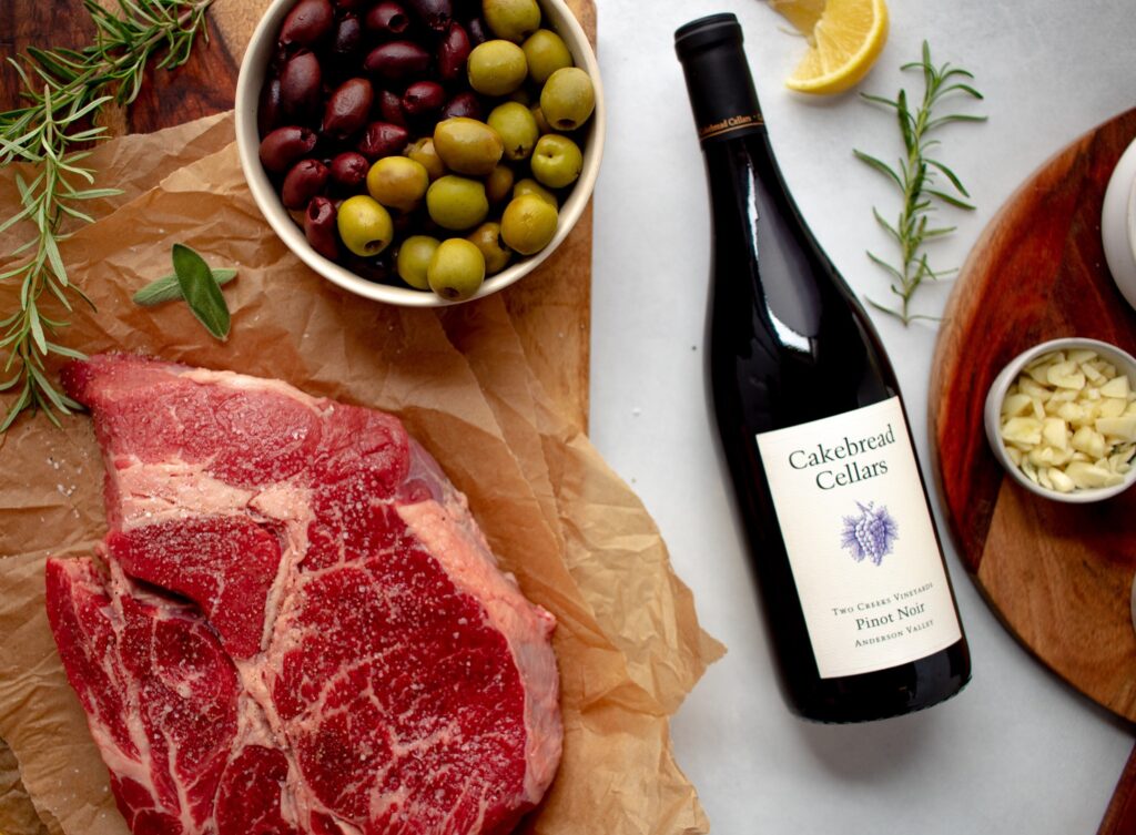 Ingredients of Italian Braised Beef and Olives. Shows the raw meat, olives, fresh herbs, garlic and Cakebread Cellars wine.
