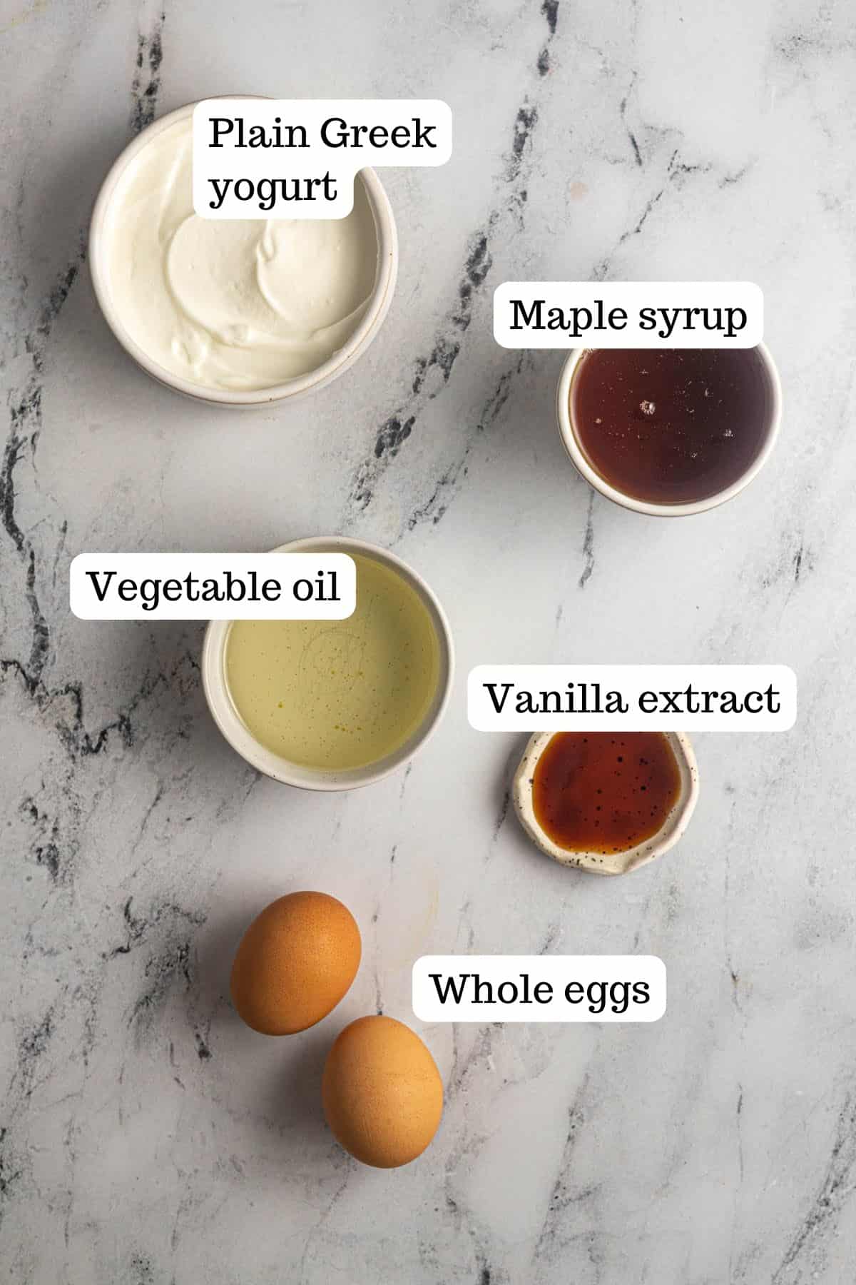 This image shows the wet ingredients for the Gluten Free Raspberry Muffins. In the bowls, you will find Greek yogurt, maple syrup, vegetable oil, vanilla extract, and whole eggs.