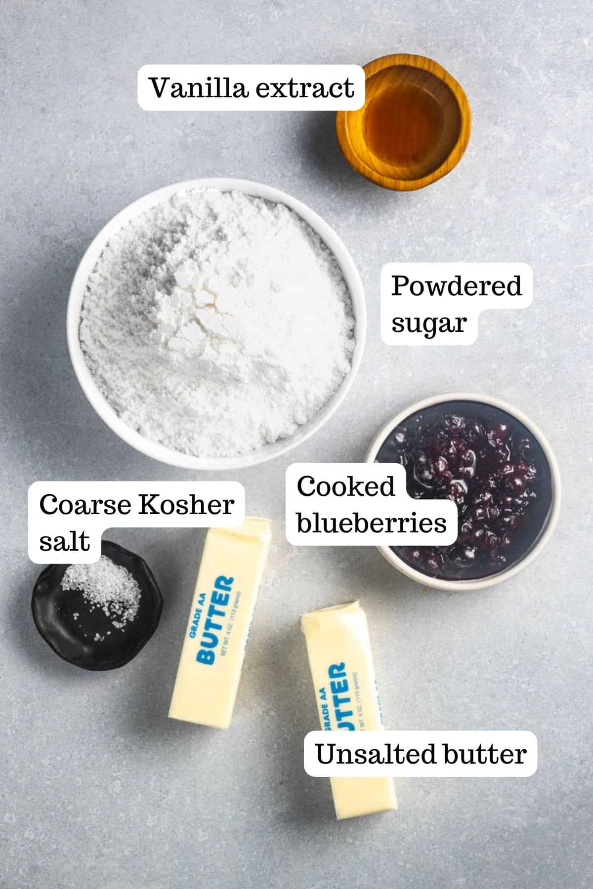 Ingredients for blueberry frosting. In the photo there are bowls of vanilla extract, powdered sugar, cooked blueberries, and kosher salt, along with 2 sticks of unsalted butter.