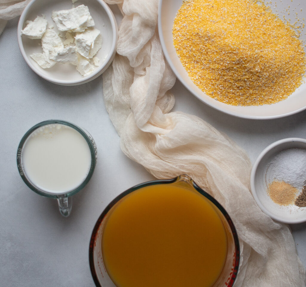 Ingredient bowls with crumbled goat cheese, dry, uncooked polenta, milk, vegetable broth, salt, pepper, and garlic powder